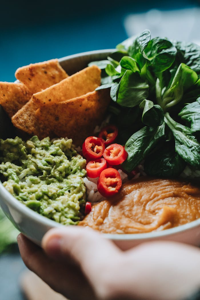 A colorful vegan buddha bowl featuring guacamole, veggies, and tortilla chips.