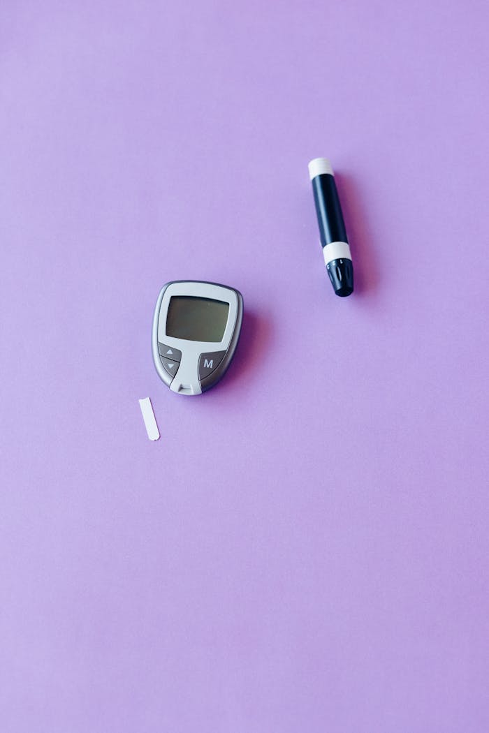 Flat lay of glucose monitor and lancet on a purple background for diabetes management.